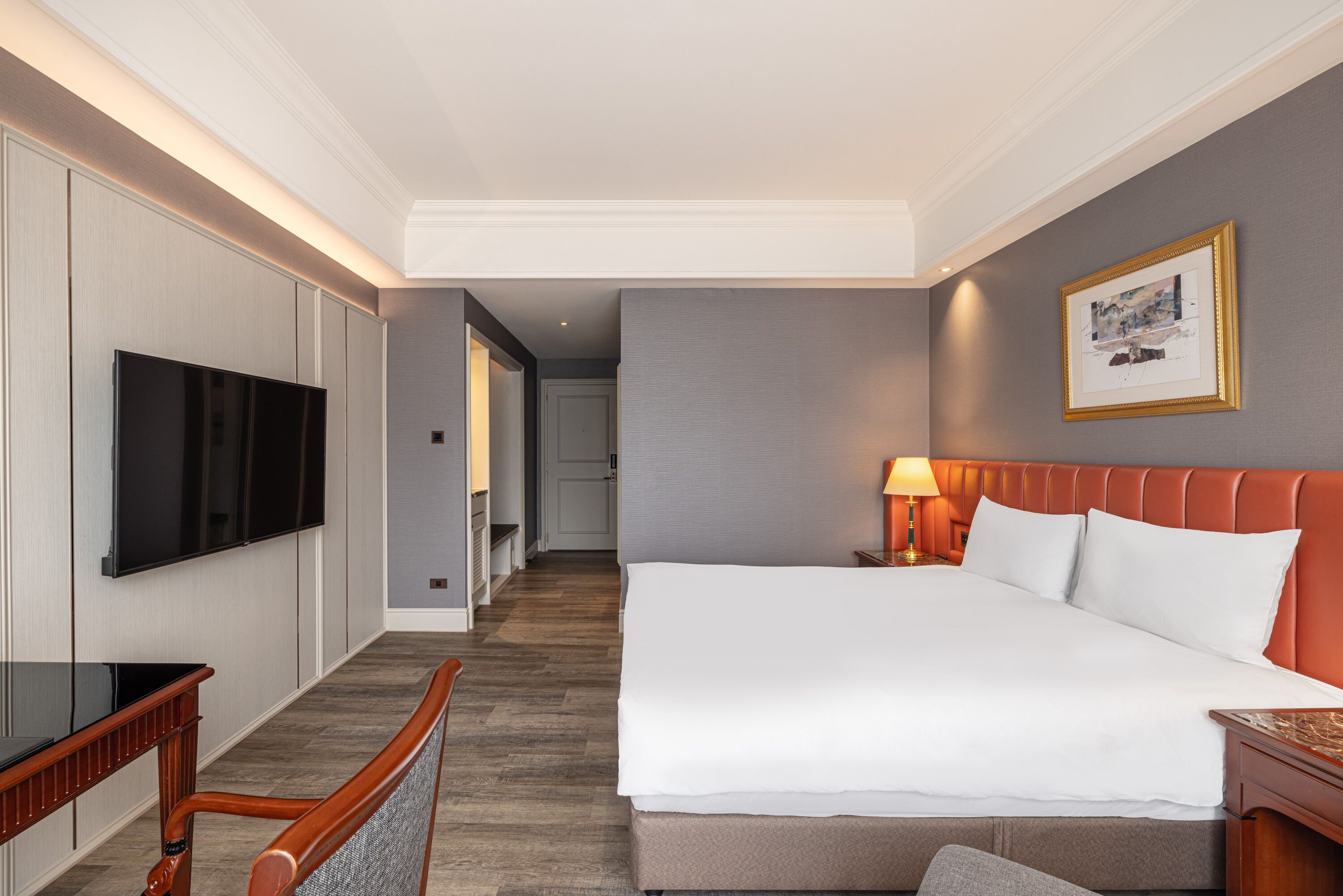 Habitación de hotel con una cama grande, un televisor de pantalla plana montado en la pared, un escritorio de madera y una silla.