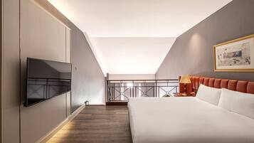 A modern hotel room with a large bed, a flat-screen TV mounted on the wall, a balcony with a railing, and a painting on the wall.