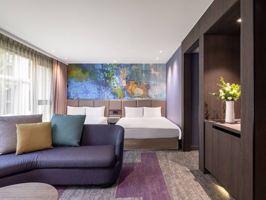 A modern hotel room with a large bed, a sofa, and a desk.