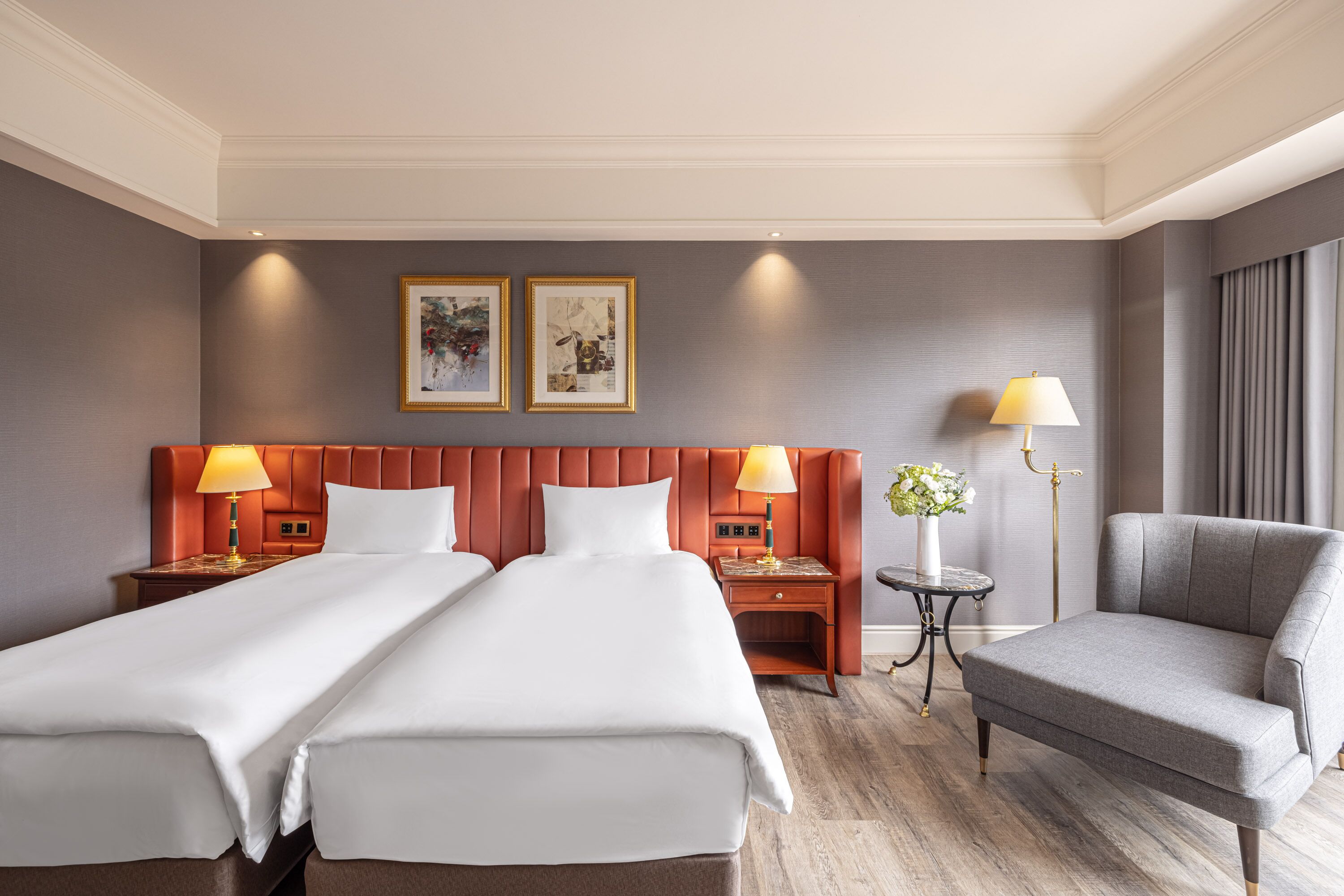 Una habitación de hotel con dos camas, un sofá, una mesita con lámpara y obras de arte en la pared.
