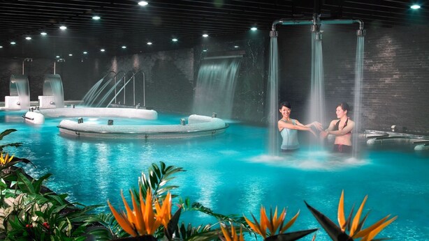 Uma área de spa com uma grande piscina interior, várias banheiras de hidromassagem e uma cascata.