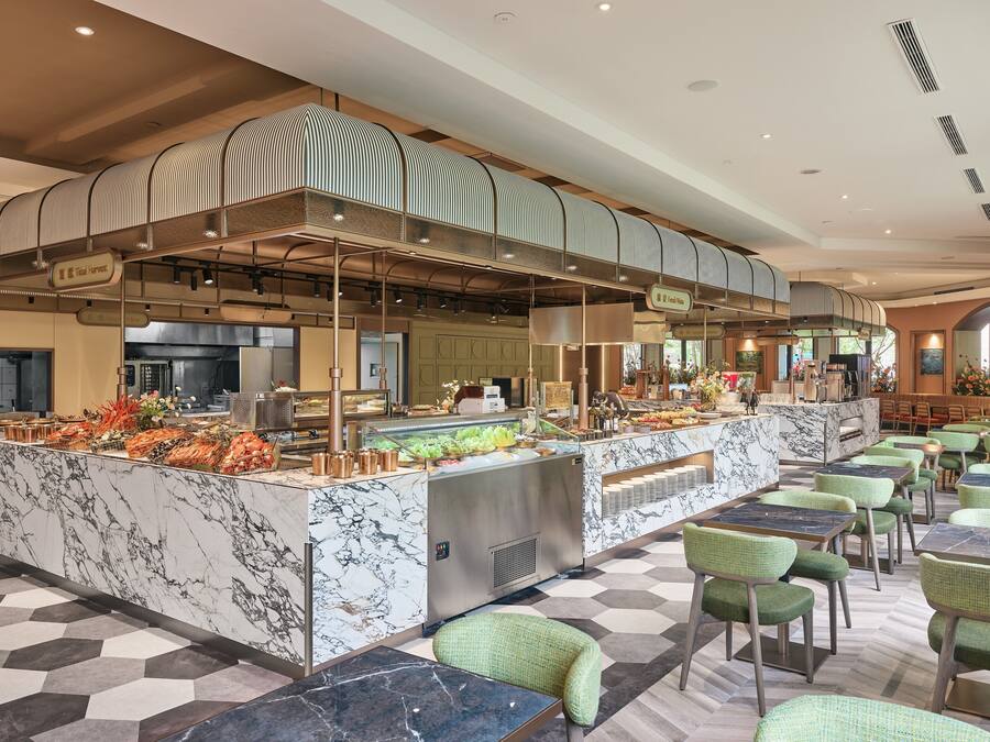 Un hall d’hôtel moderne avec un comptoir d’accueil en marbre, un espace buffet et des fauteuils recouverts d’un tissu vert.