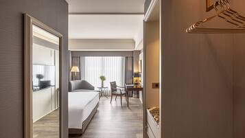 A hotel room with a bed, a desk, a chair, a lamp, and a mirror.