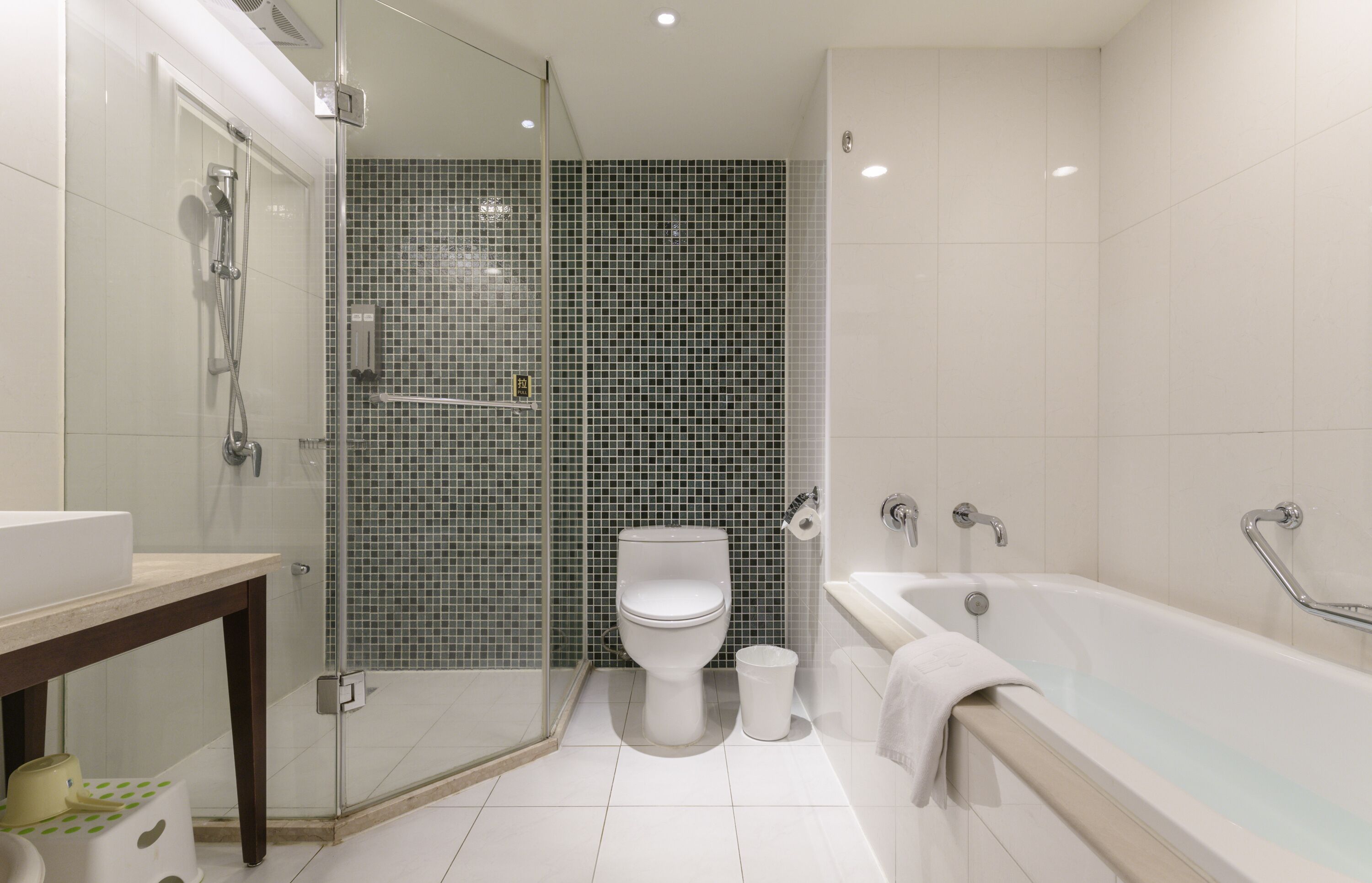 Een moderne badkamer met een douchecabine van glas, een wit toilet en een bad met een handgreep.