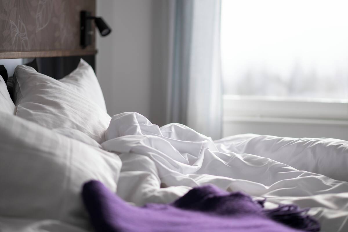 Un lit avec une literie blanche et une couverture violette, une tête de lit en bois et une fenêtre donnant sur un beau paysage.