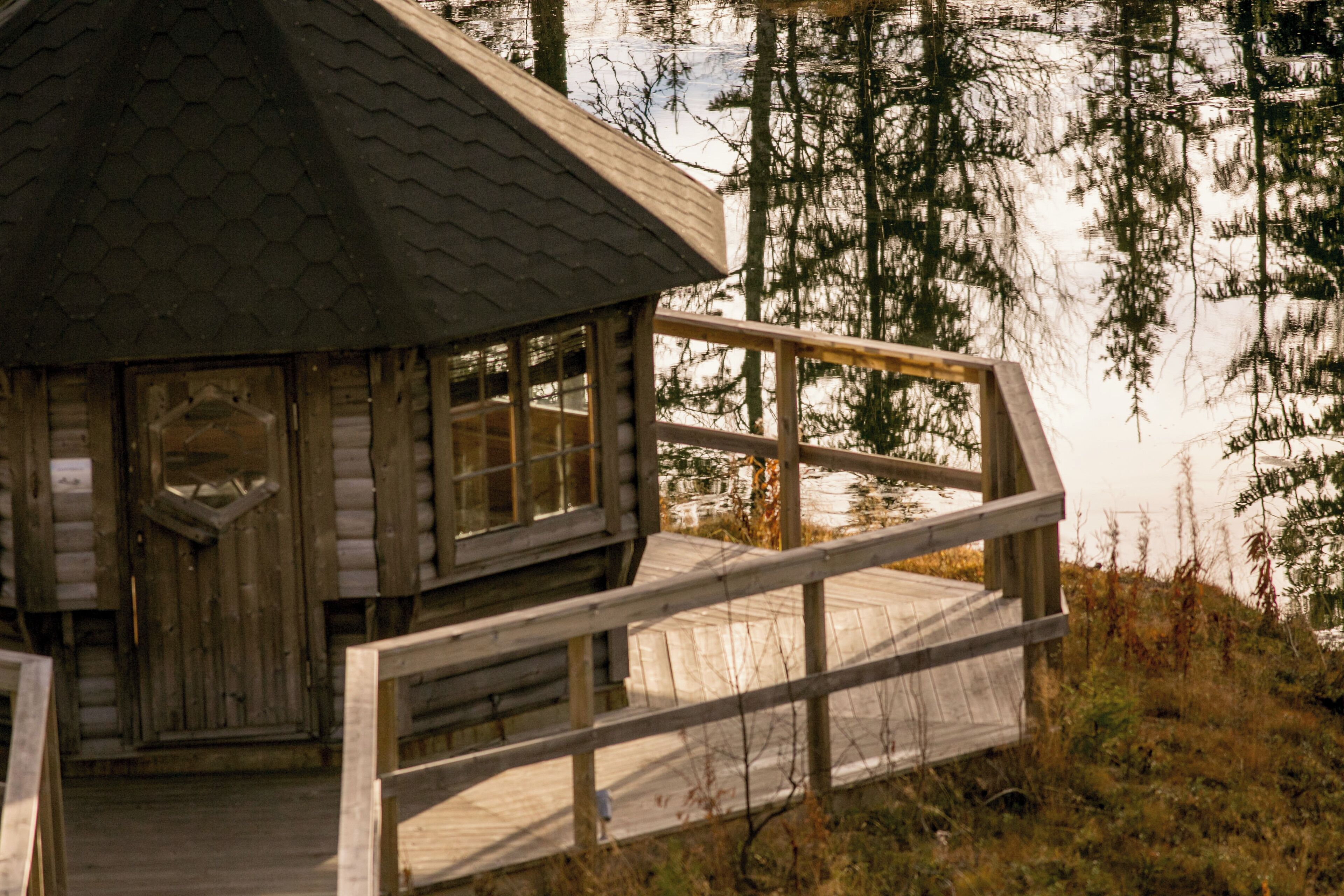 Una cabaña de madera con techo hexagonal, una terraza de madera y vistas a un área boscosa.