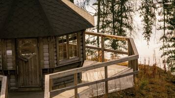 Una cabaña de madera con techo hexagonal, una terraza de madera y vistas a un área boscosa.