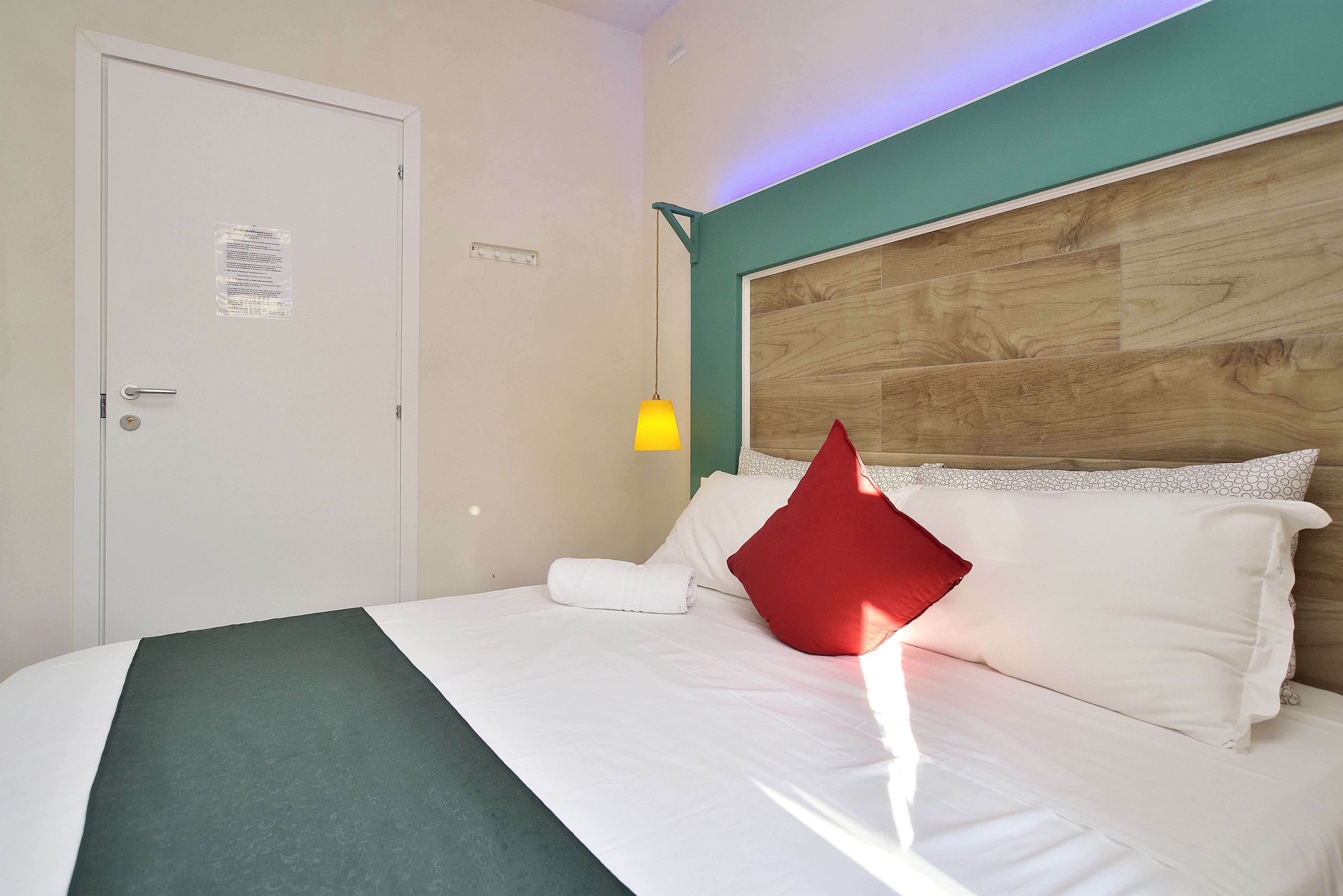 Habitación de hotel con cabecera de madera, ropa de cama blanca, pared de acento verde y una lámpara colgante amarilla.