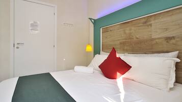 Habitación de hotel con cabecera de madera, ropa de cama blanca, pared de acento verde y una lámpara colgante amarilla.