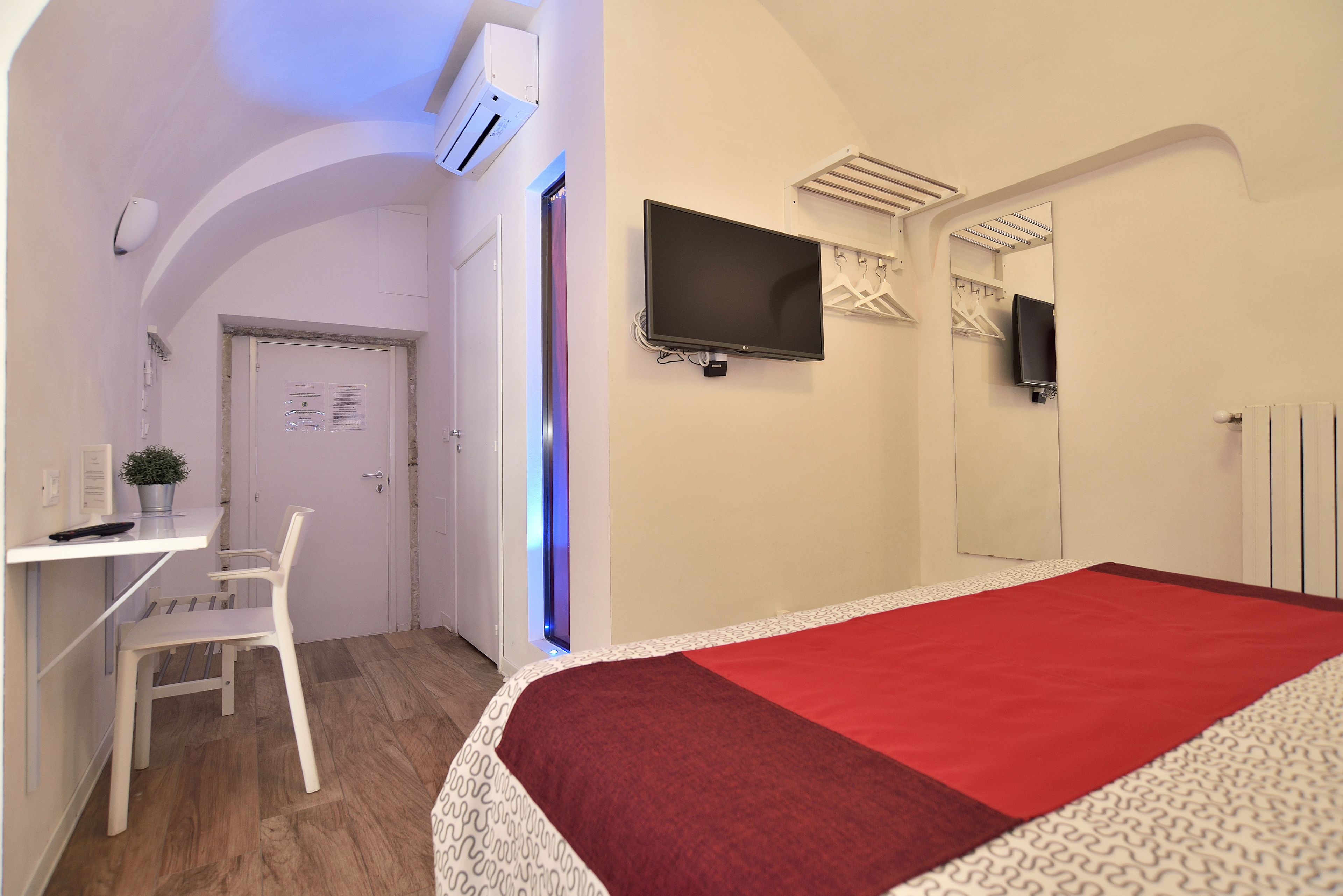 A hotel room with a bed, a desk, a chair, a TV, and a wardrobe.