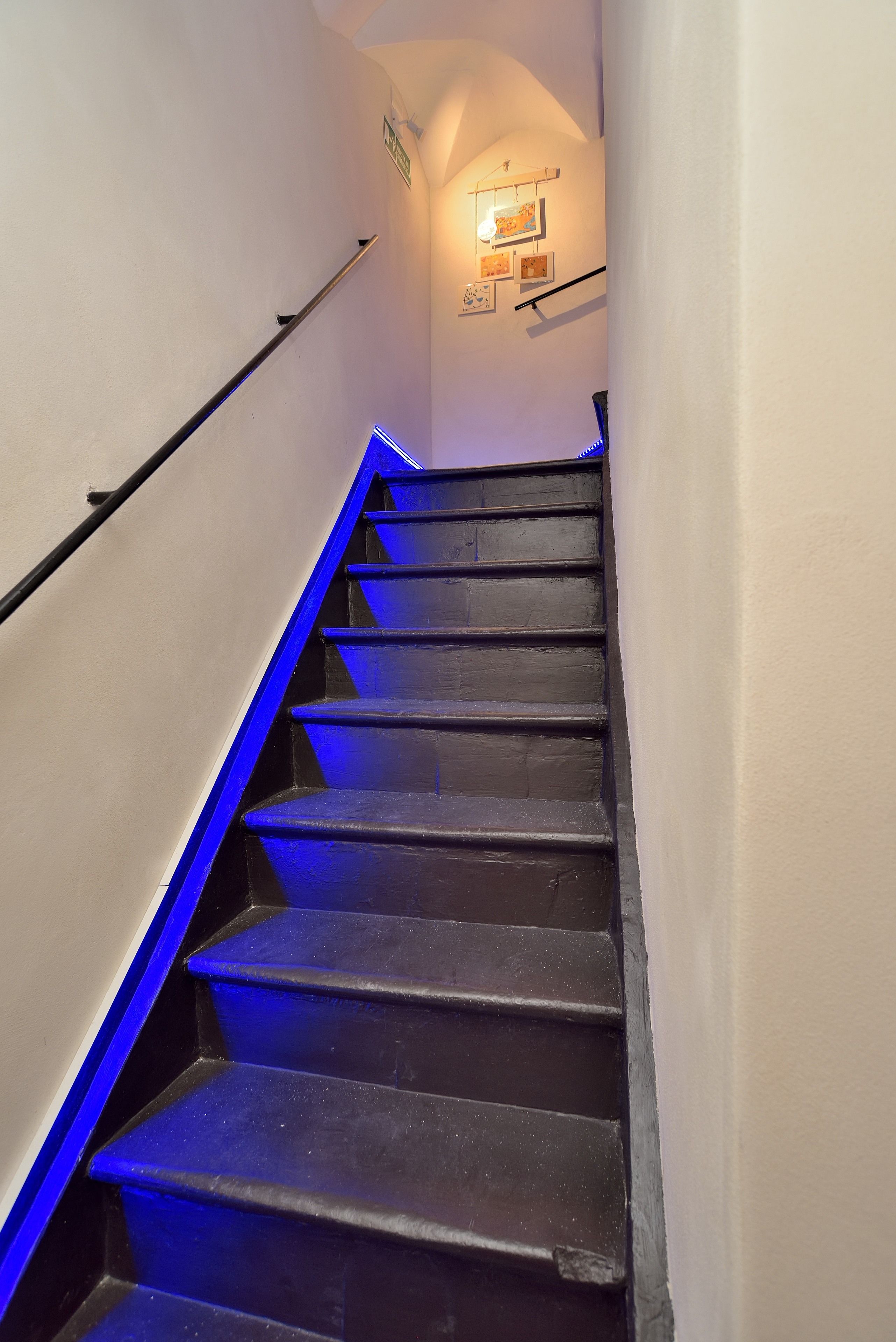 Een trap met blauwe verlichting, leuningen en een wandlamp.