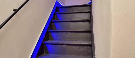 Una escalera con iluminación azul, barandales y una lámpara en la pared.