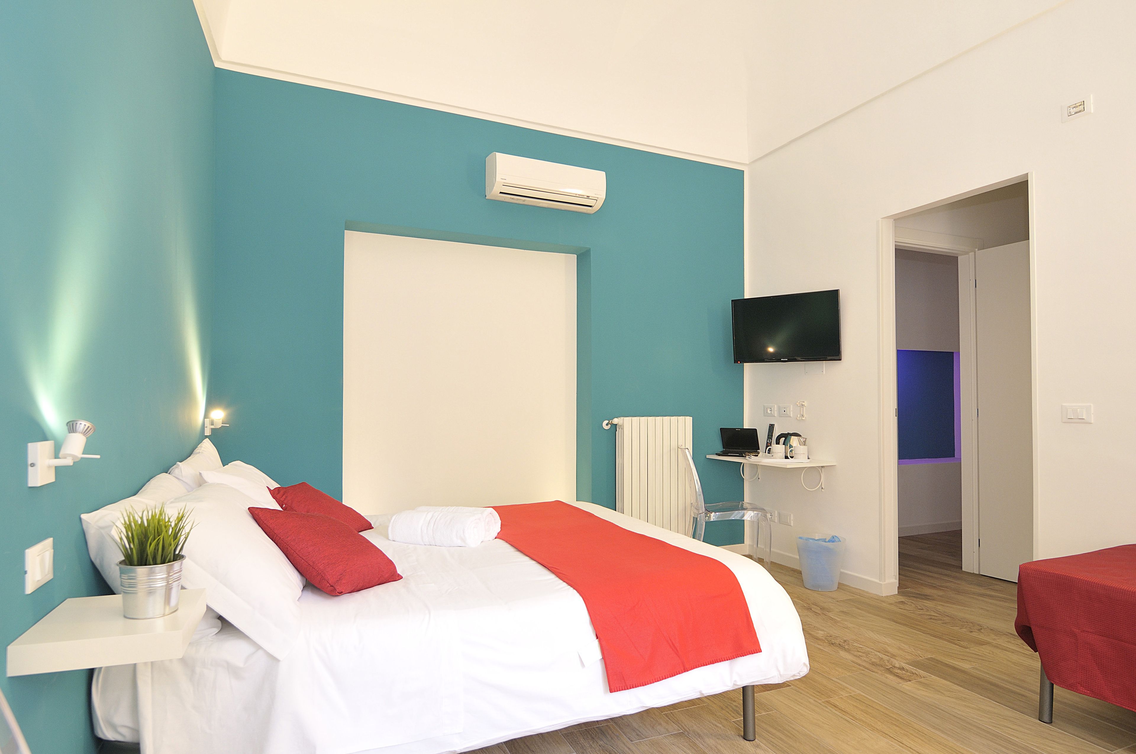 A modern hotel room with a bed, a TV, a desk with a computer, and a bathroom visible through an open door.