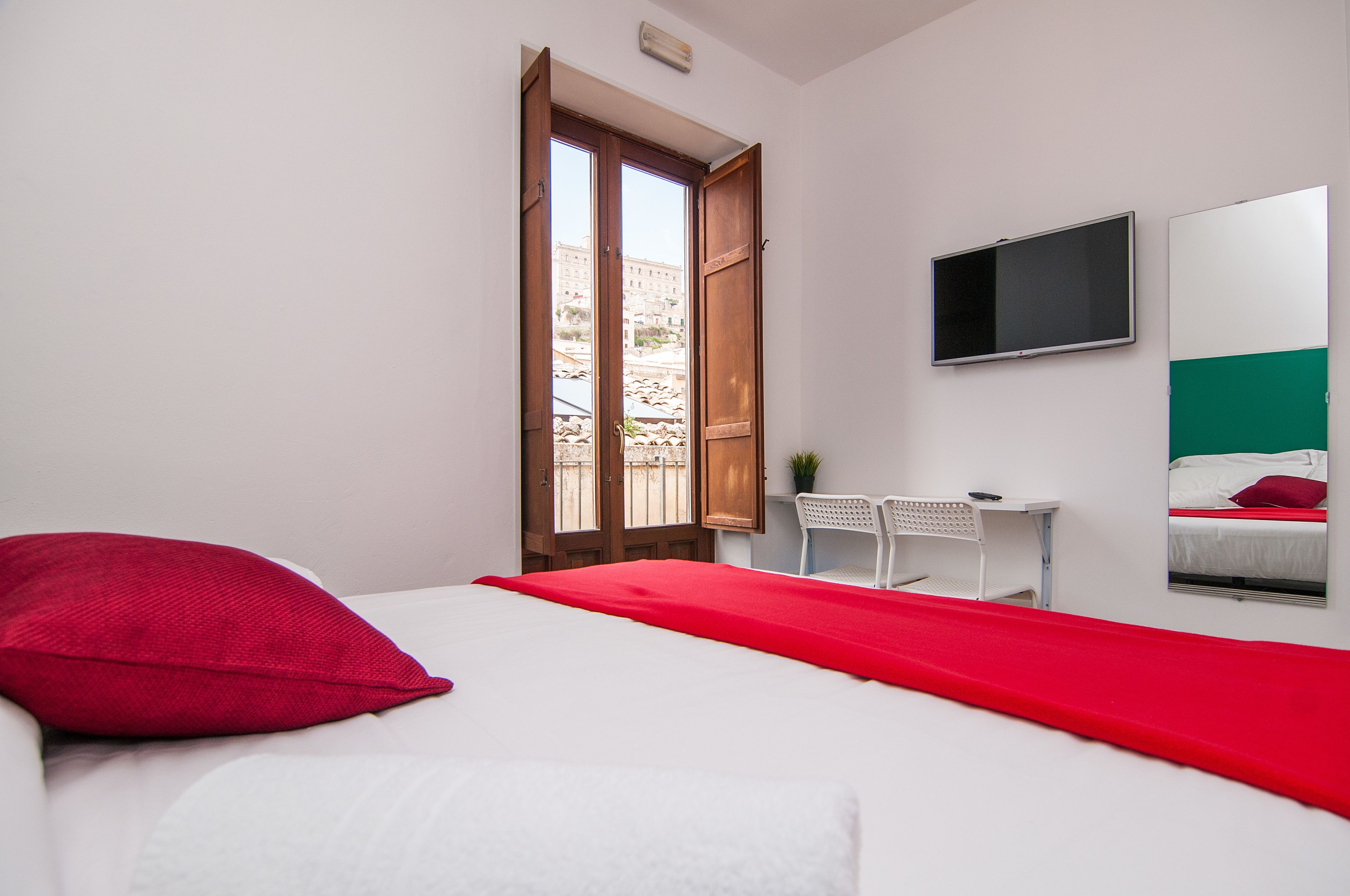 Una camera da letto con un letto, una scrivania, una sedia, una TV e una finestra con porta aperta.