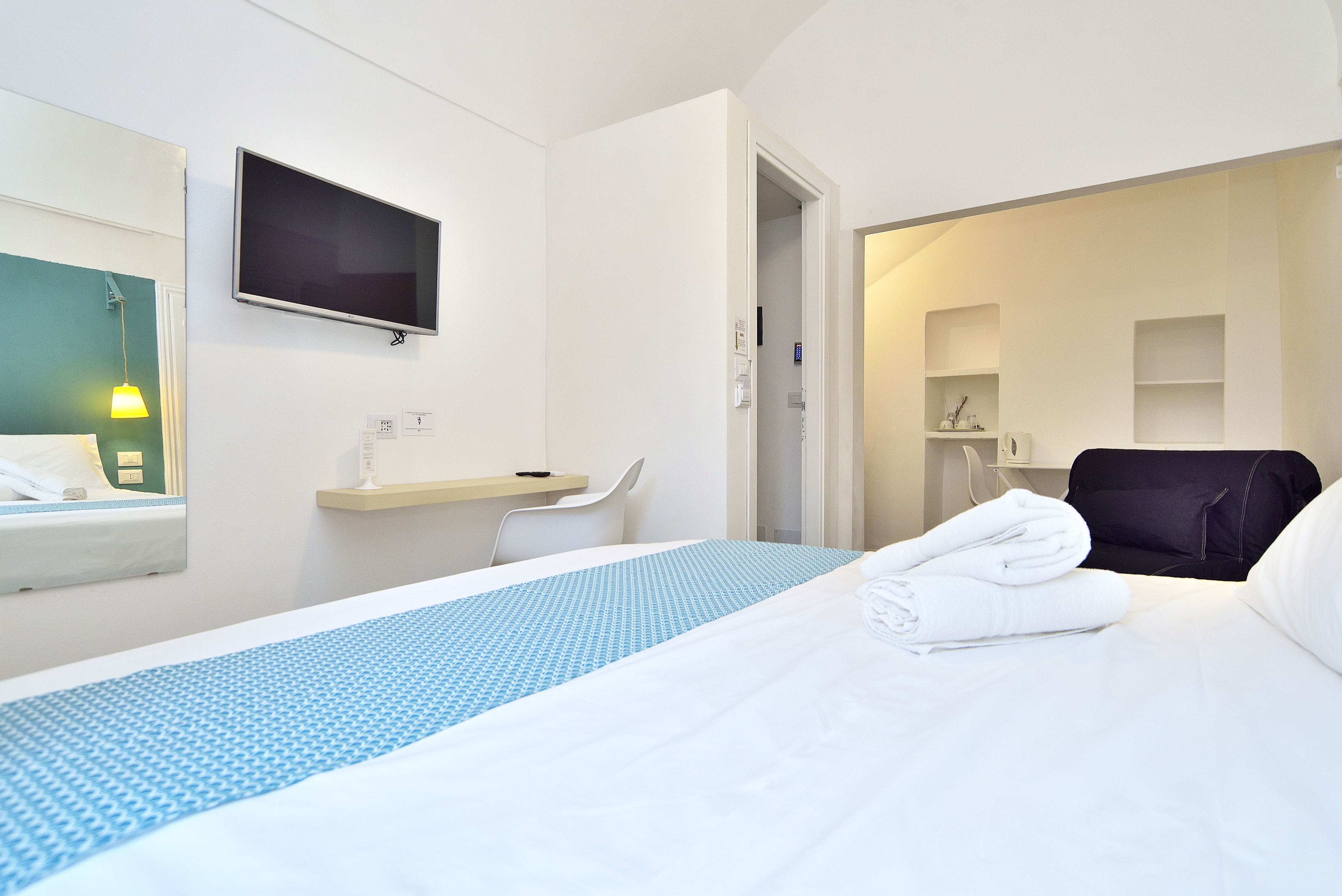 Habitación de hotel con una cama, escritorio, silla, televisor y baño visible a través de una puerta abierta.