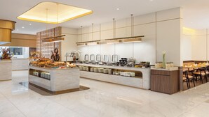 A modern hotel lobby with a marble reception desk, buffet area, and seating arrangement. - Atria Hotel Malang (Malang)