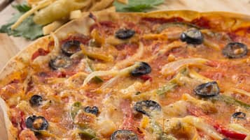 A pizza with various toppings, a side of fries, and a small bowl of ketchup on a wooden board.