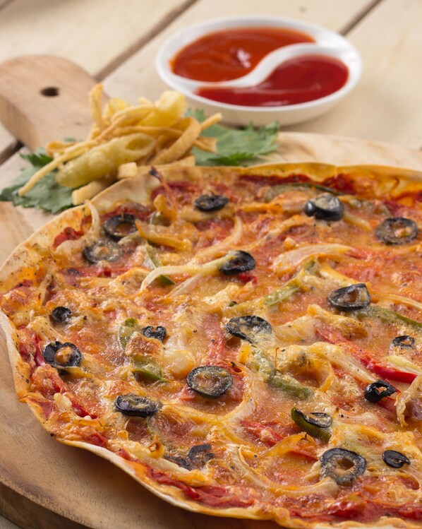 A pizza with various toppings, a side of fries, and a small bowl of ketchup on a wooden board.