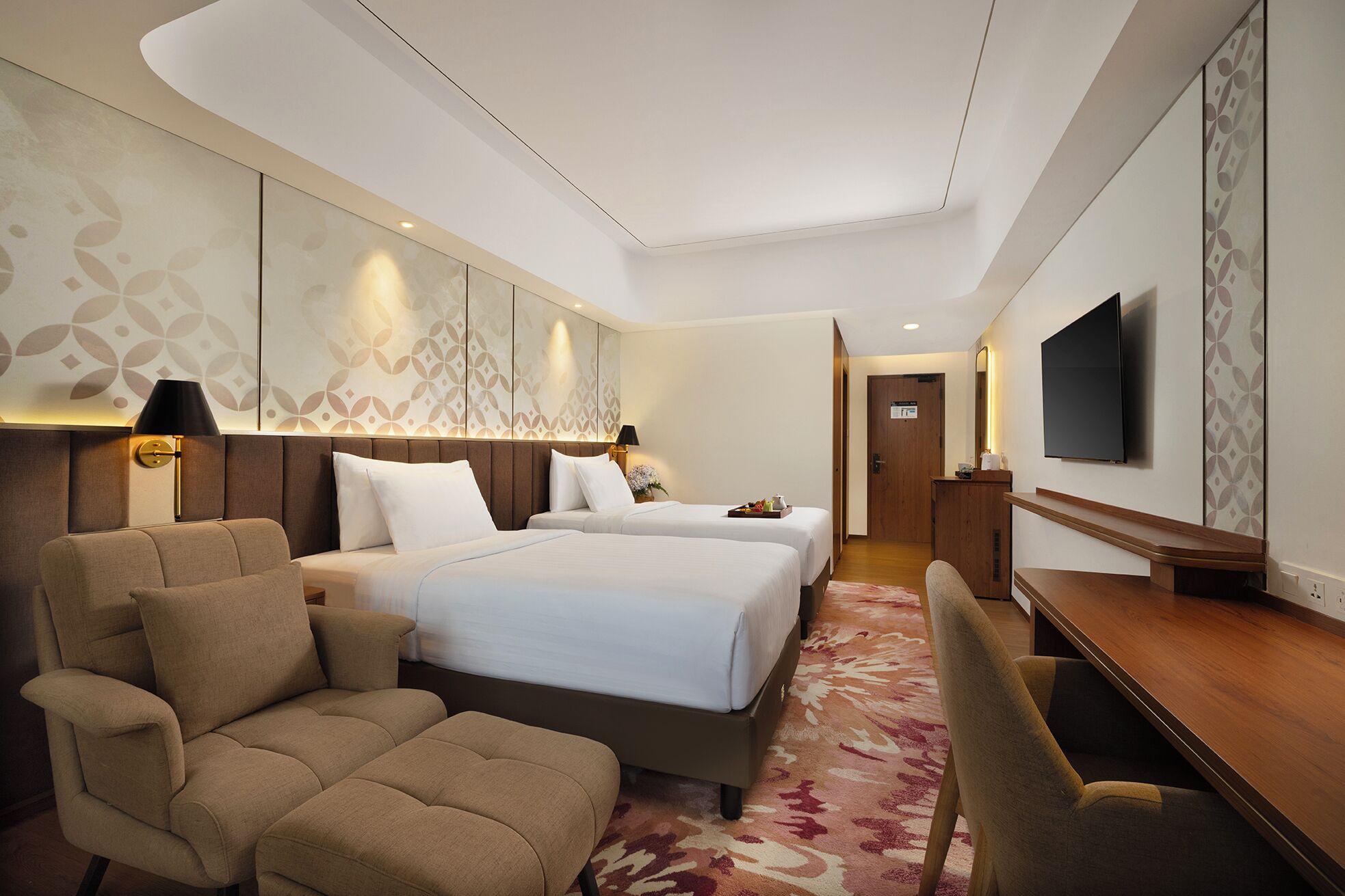 A hotel room with two beds, a sofa, a desk, and a TV.