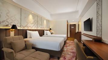 A hotel room with two beds, a sofa, a desk, and a TV.