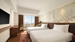 A hotel room with two beds, a desk, a chair, a TV, and a large window with a view. - Atria Hotel Malang (Malang)