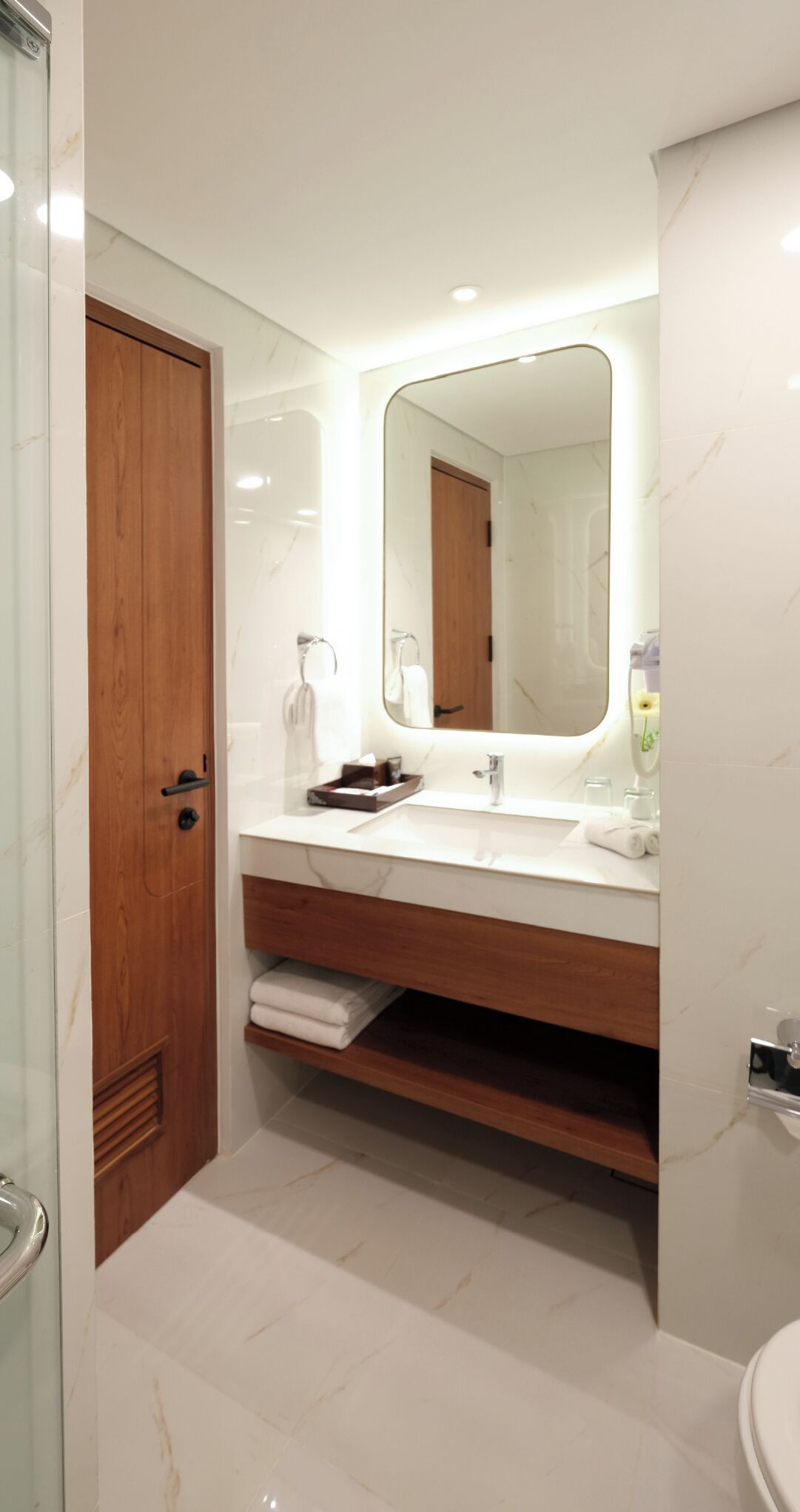 A modern bathroom with a wooden vanity, a large mirror, and a glass shower enclosure.