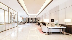 A modern hotel lobby with a reception desk, seating area, and a view into the dining area. - Atria Hotel Malang (Malang)