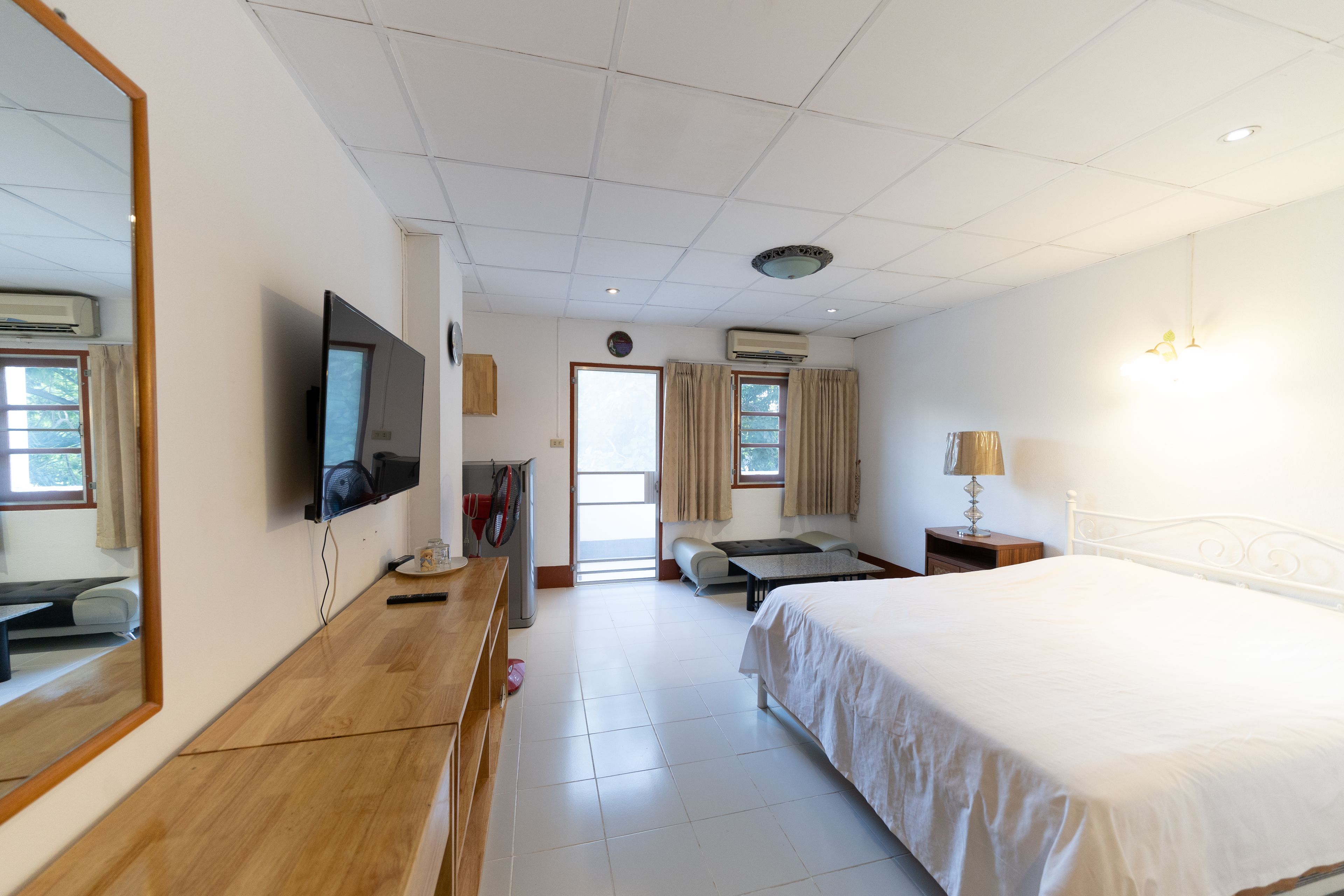 Une chambre d’hôtel équipée d’un lit, d’un bureau, d’une télévision, d’un miroir, d’une fenêtre avec des rideaux et d’un appareil de climatisation.