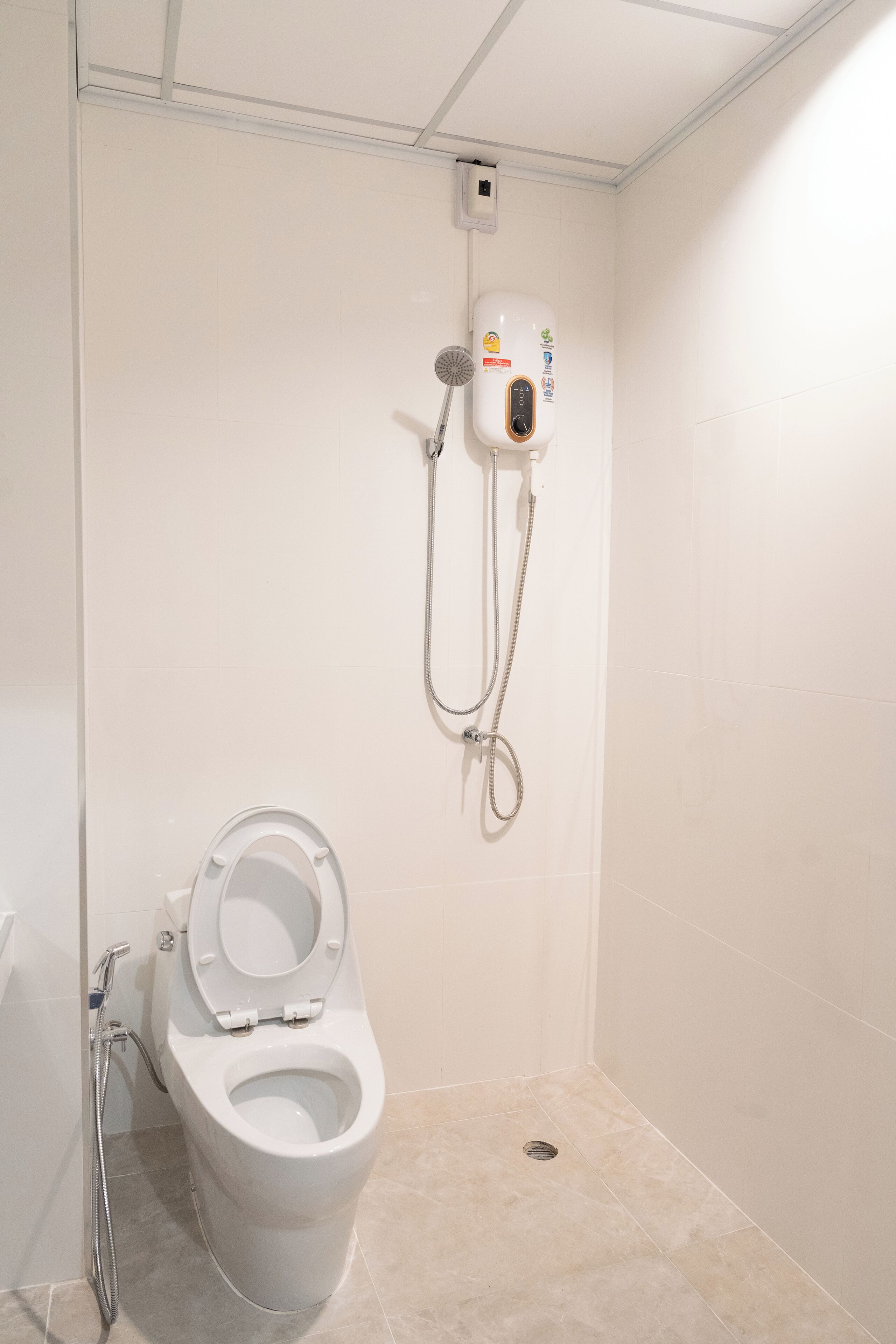 A small, modern bathroom with a toilet, a shower, and a wall-mounted control panel.