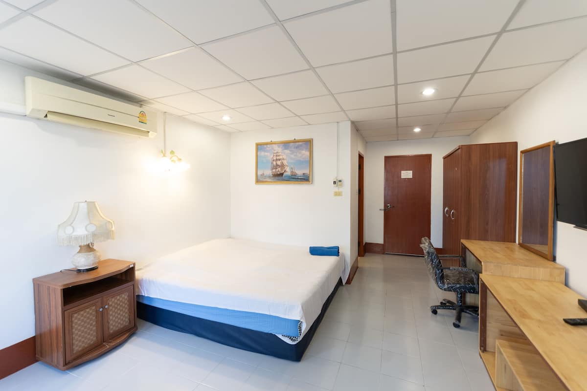 A hotel room with a bed, a desk, a chair, an air conditioner, a lamp, a painting, and a wardrobe.