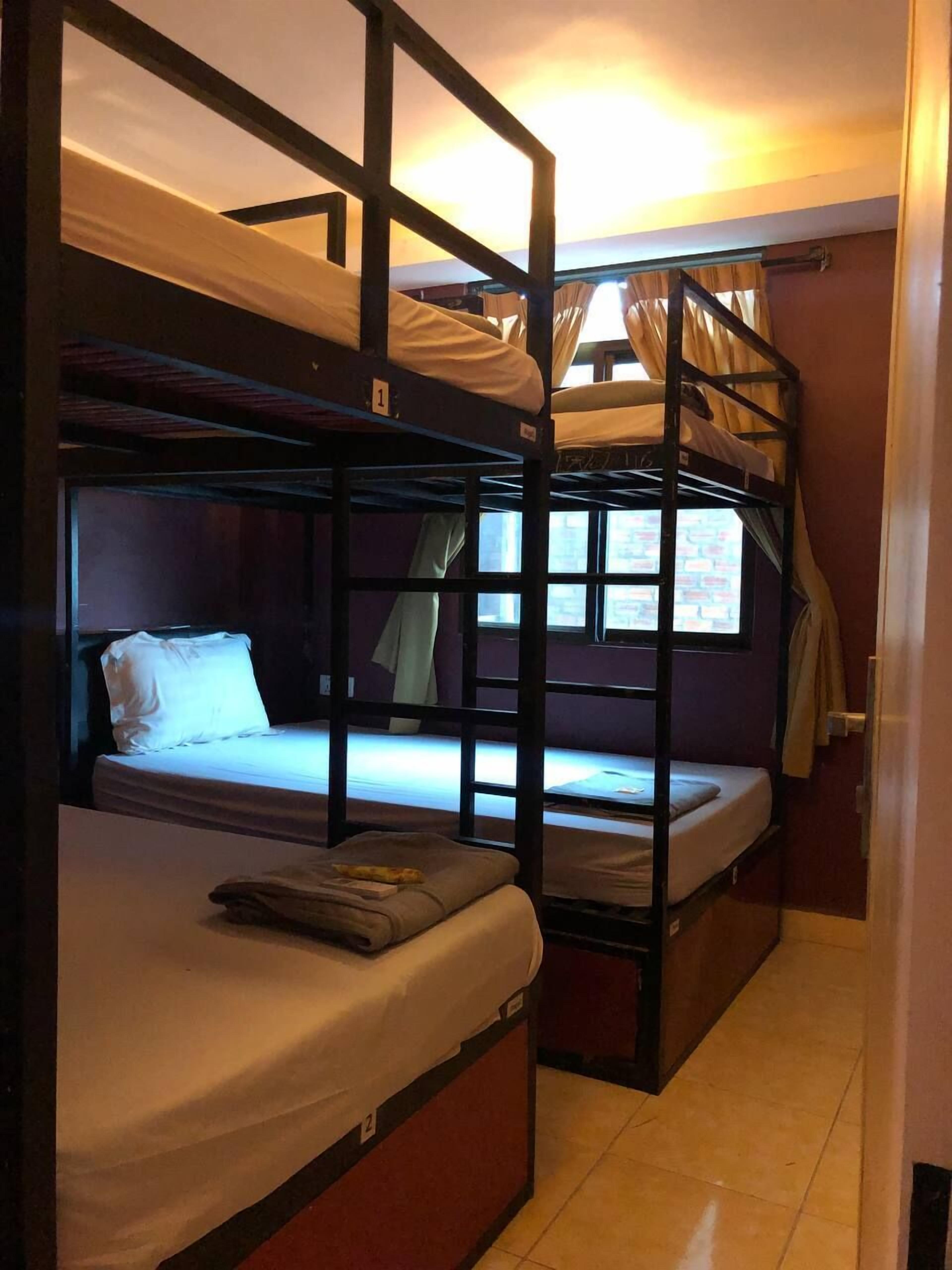 A dormitory room with bunk beds, a window with curtains, and a tiled floor.