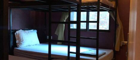 A dormitory room with bunk beds, a window with curtains, and a tiled floor.