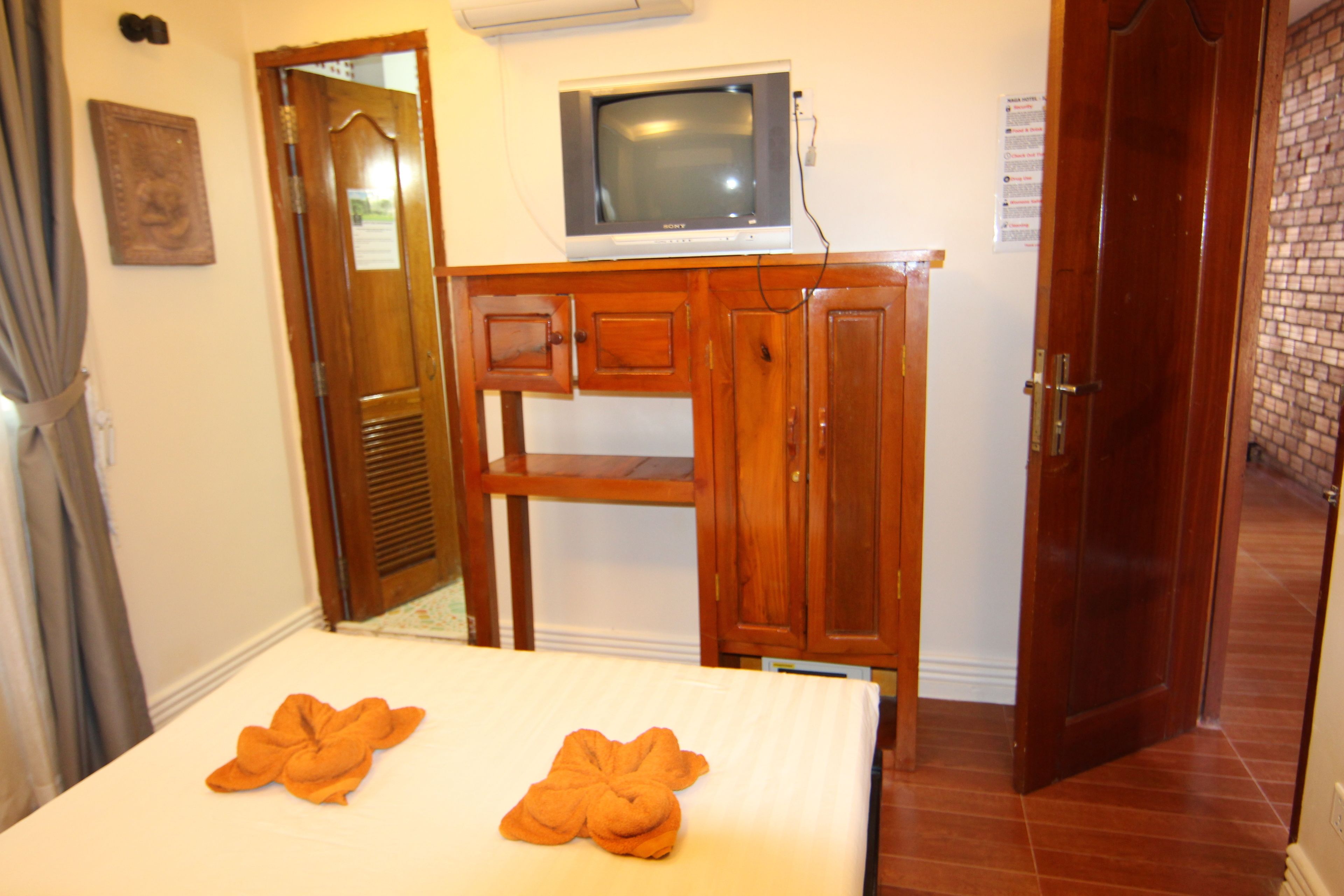 A hotel room with a bed, a wooden cabinet, a television, and a door.