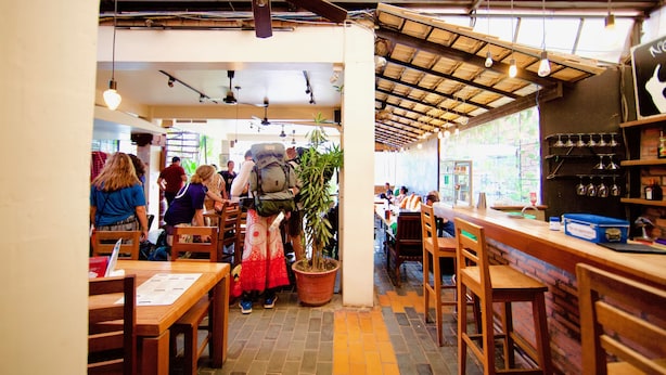 Interior de restaurante con mesas y sillas de madera, un ventilador de techo y una planta en maceta.