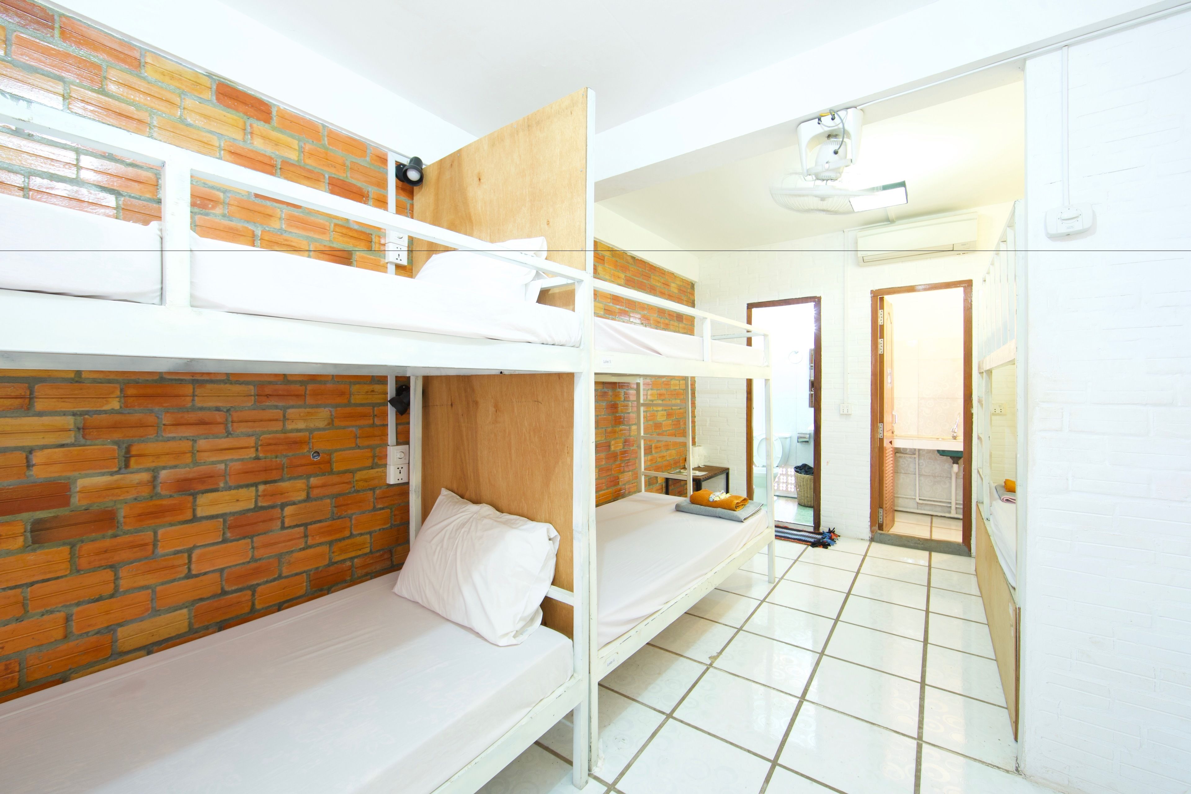 Een slaapzaal met stapelbedden, een bakstenen muur en een betegelde vloer.