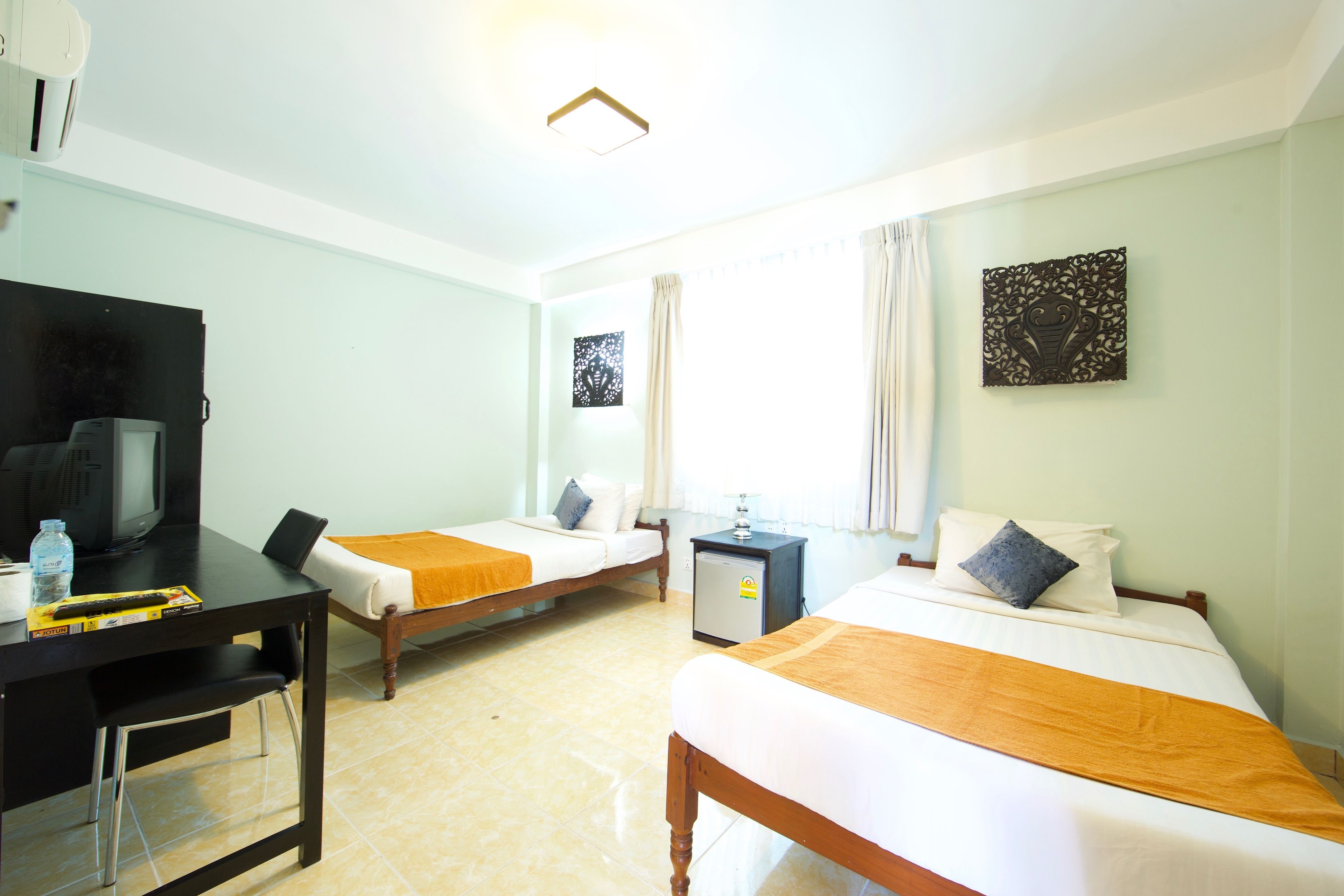 A hotel room with two beds, a desk with a television, a small refrigerator, and a window with curtains.