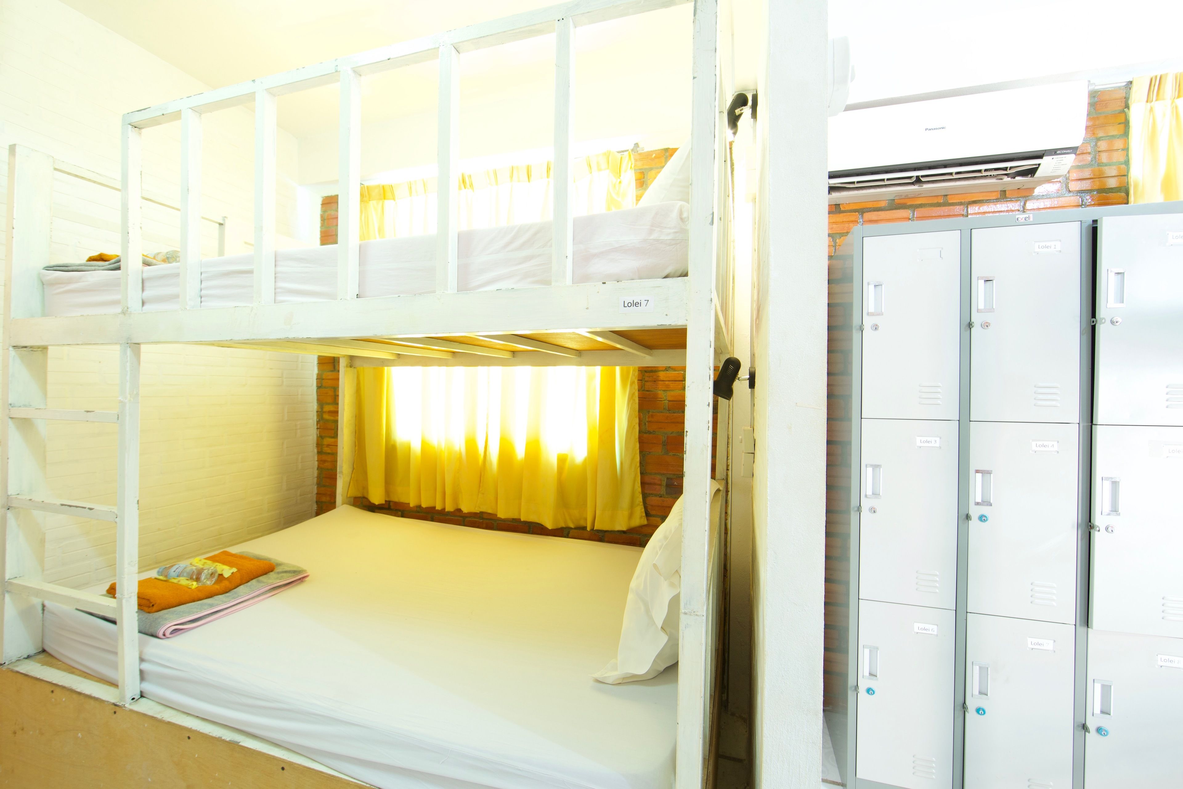 A bunk bed room with a brick wall, a window with yellow curtains, and a set of lockers.