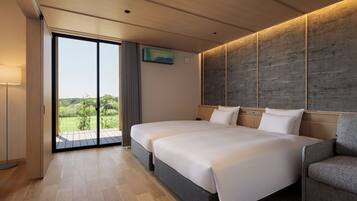 A modern hotel room with two beds, a large sliding glass door to a balcony, and a view of greenery.