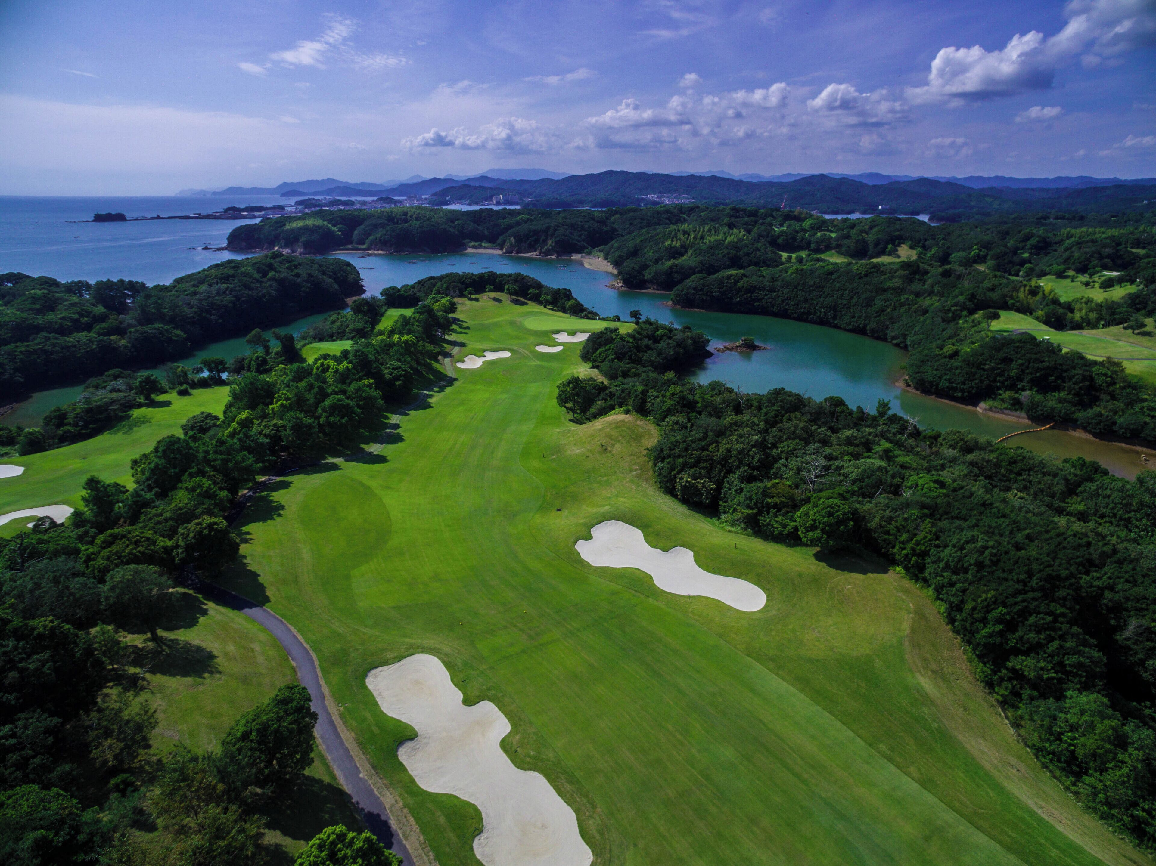 An aerial view of a golf course with sand bunkers, a water body, and surrounding greenery.