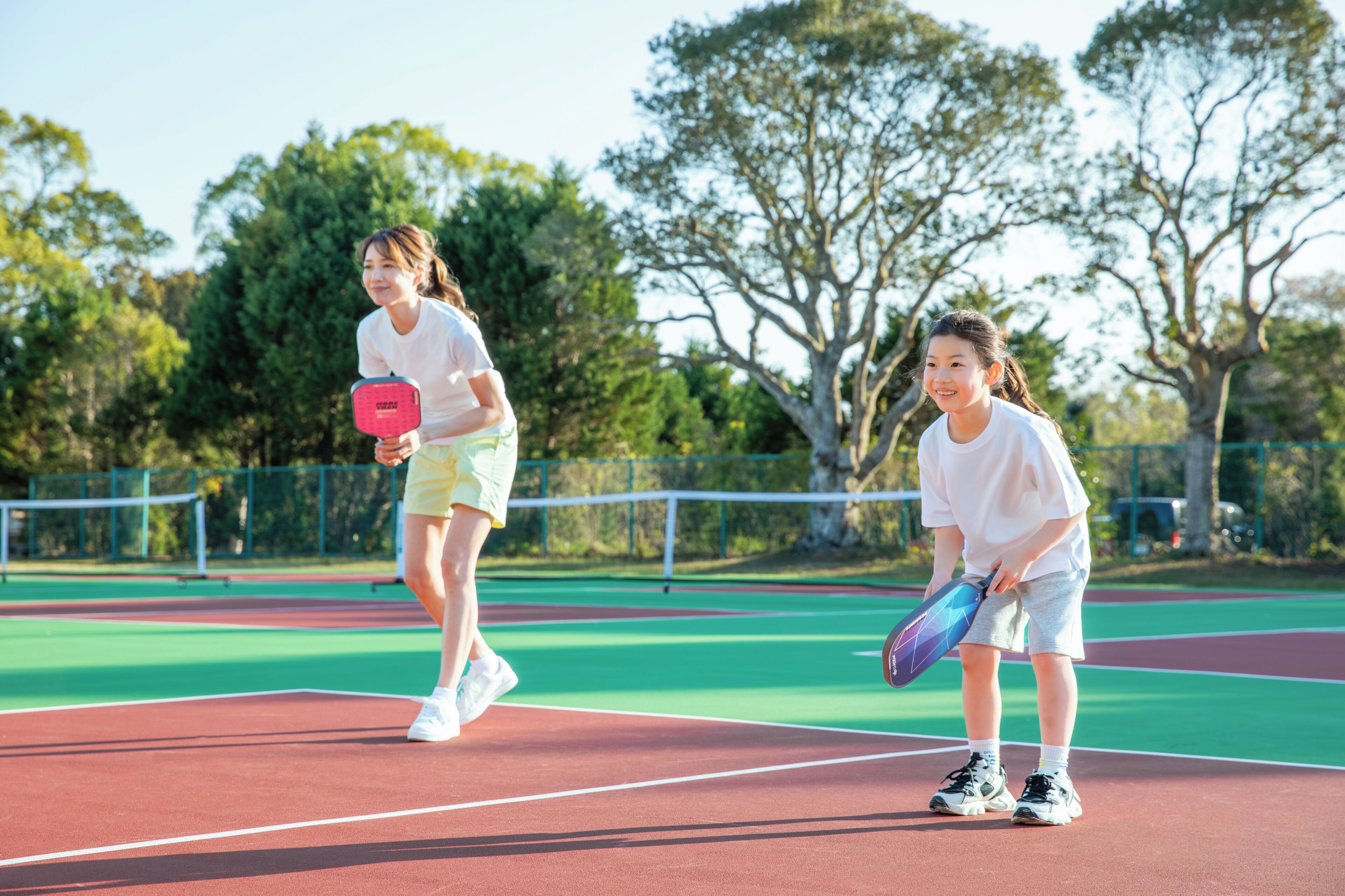 Two people on a tennis court with trees in the background.