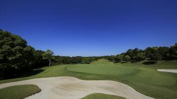 A golf course with sand bunkers, green fairways, and dense trees.