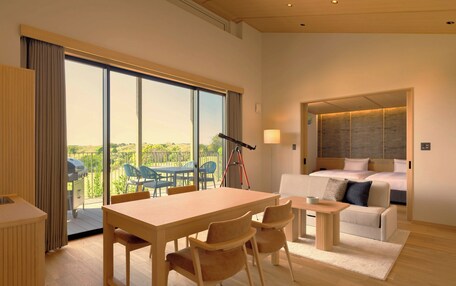 A modern hotel room with a large window, a dining area, a sofa, and a bed.