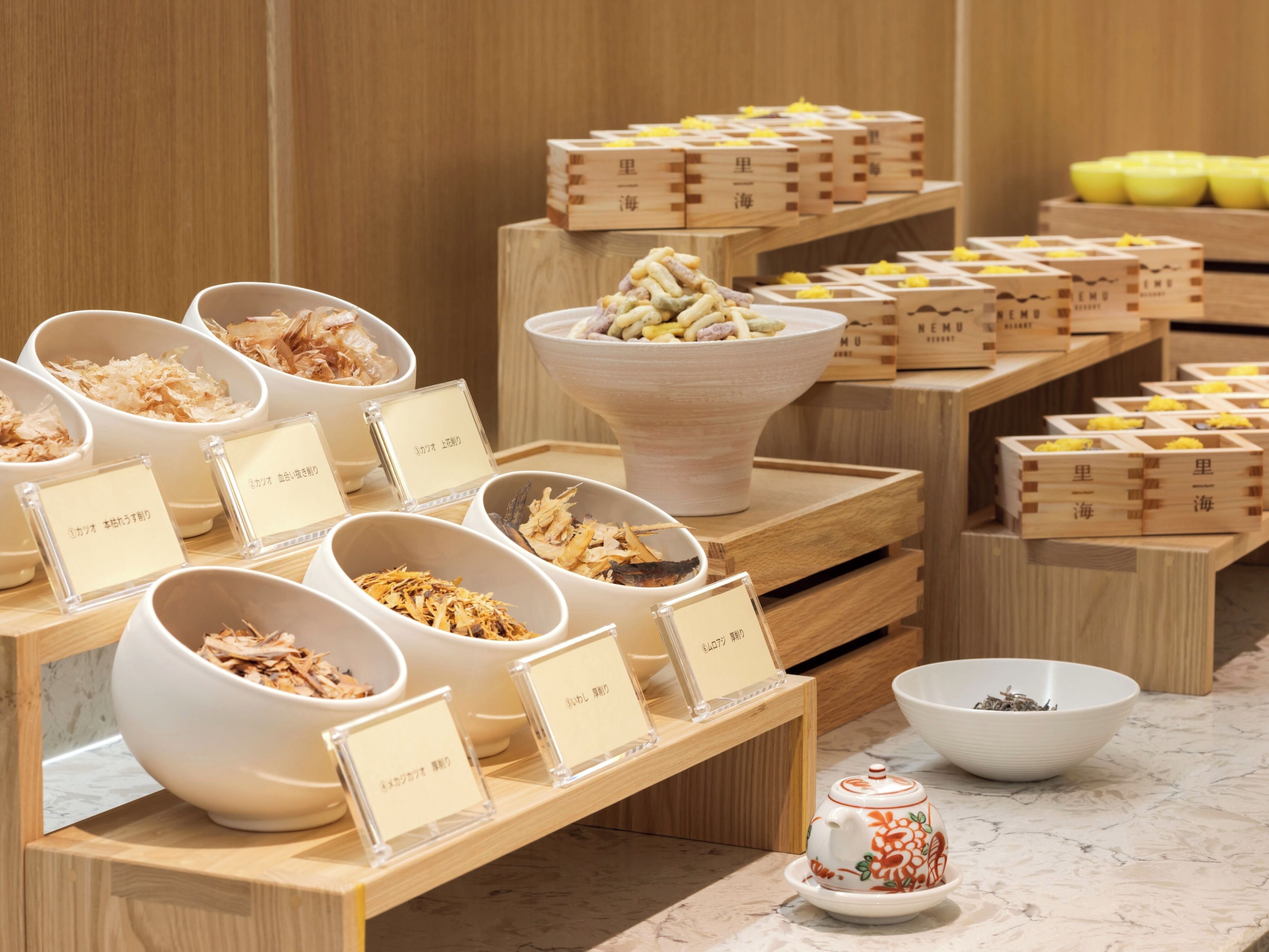 Una exhibición de diversos alimentos en recipientes con etiquetas, dispuestos sobre puestos de madera en un restaurante.