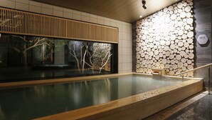 A modern indoor pool area with a wooden deck, a large window with a view of trees, and a wall decorated with circular wooden logs. - Nemu Resort Hotel Nemu (Shima)