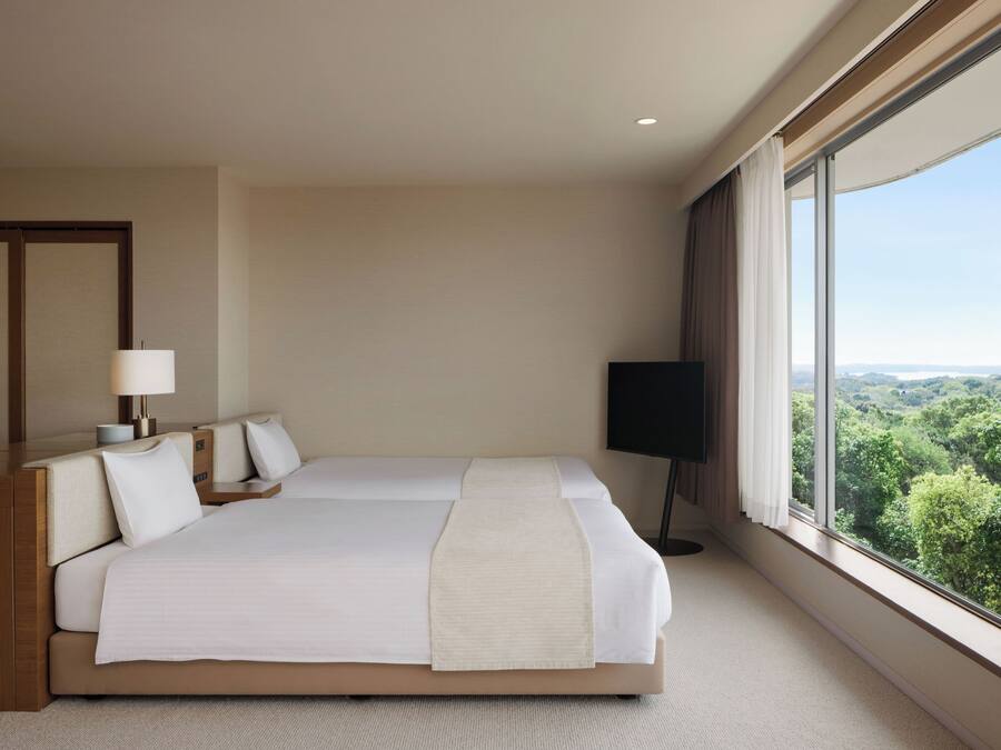 A hotel room with a large bed, a desk, a chair, a TV, and a window with a view of the landscape.