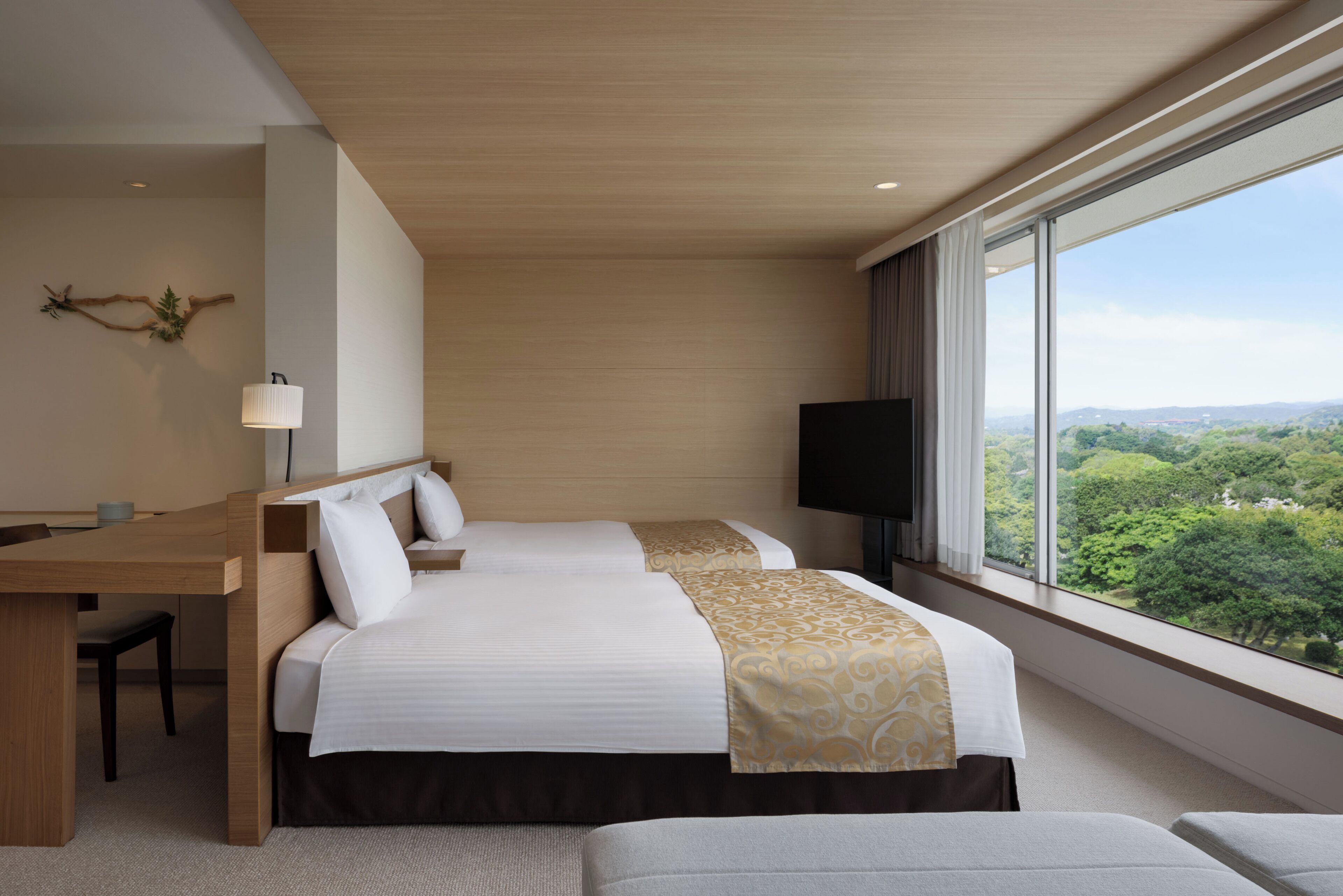 A hotel room with a bed, a desk, a chair, a TV, and a large window with a view.