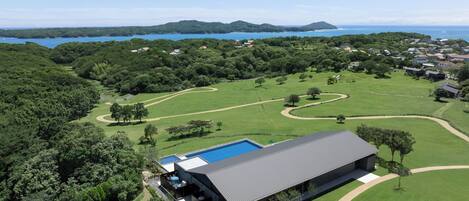 A modern house with a swimming pool, surrounded by lush greenery and a golf course.