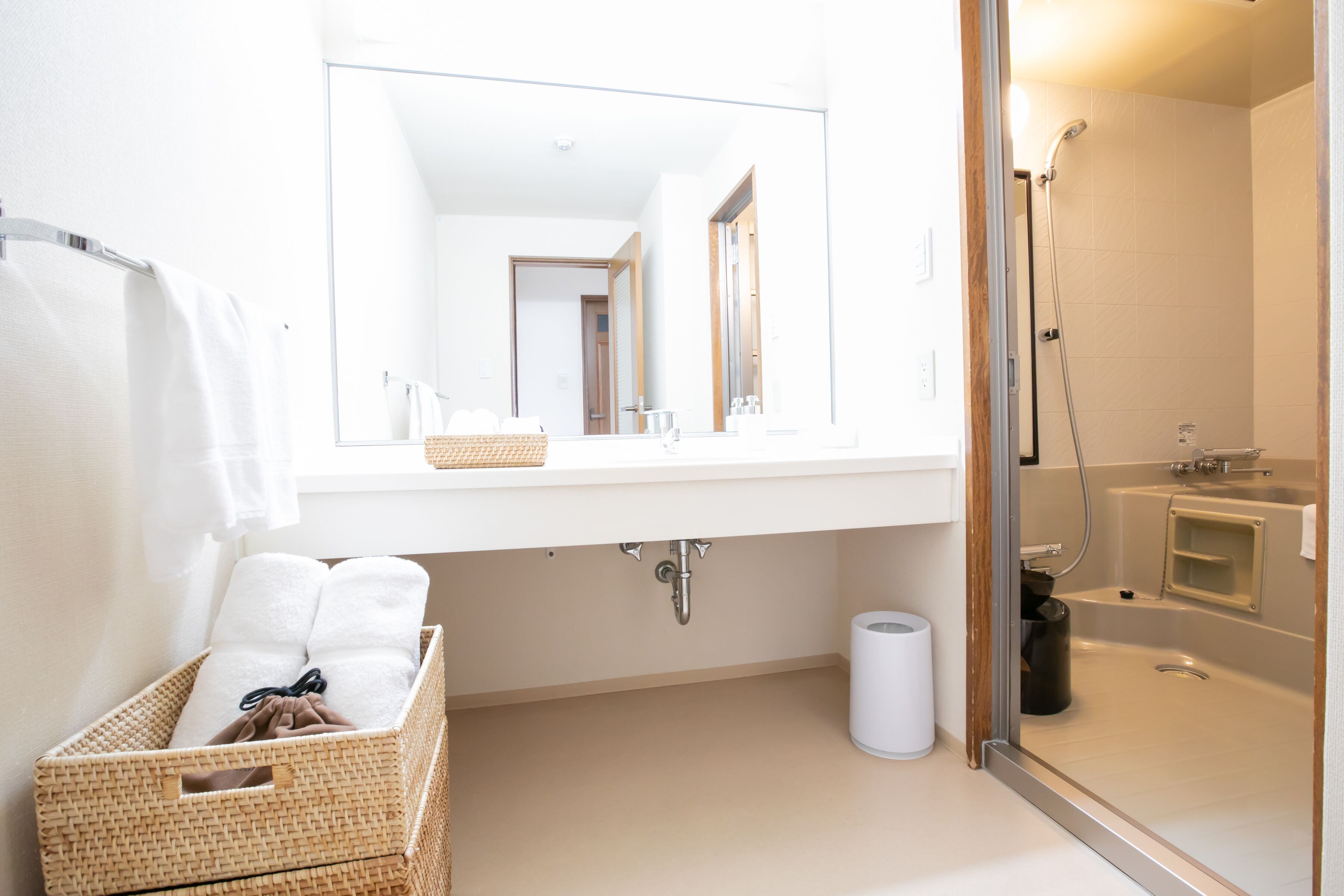 A bathroom with a white sink, a mirror, a shower, and a basket of towels.