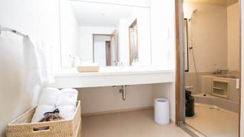 A bathroom with a white sink, a mirror, a shower, and a basket of towels.