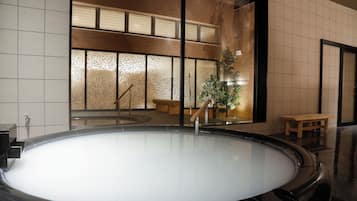A large indoor hot tub with a wooden bench and a potted plant nearby.